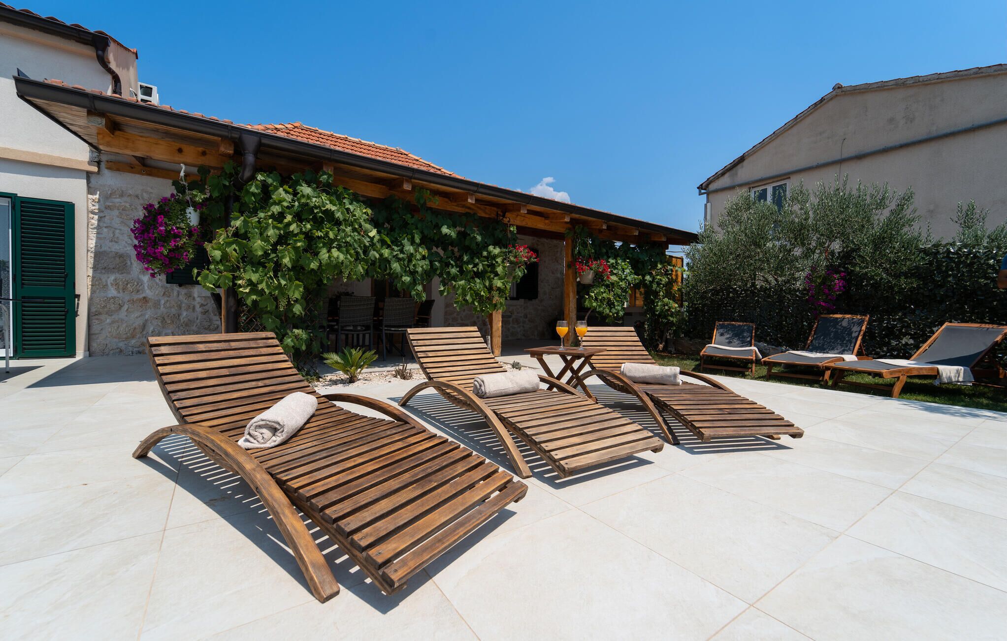 A sunlit outdoor seating area with wooden loungers and a stone wall.