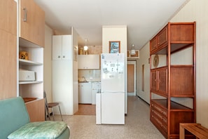 A compact kitchen with a refrigerator, cabinets, and a dining area with a chair.
