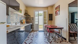 A kitchen with a tiled backsplash, a dining area with a table and chairs, and a view through an open door. - Villa 'Bikini' with Private Terrace and Private Garden (Soulac-sur-Mer)