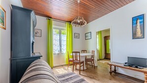A living room with a sofa, a TV on a wooden stand, a dining area with chairs and a table, and a staircase leading to another room. - Villa 'Bikini' with Private Terrace and Private Garden (Soulac-sur-Mer)
