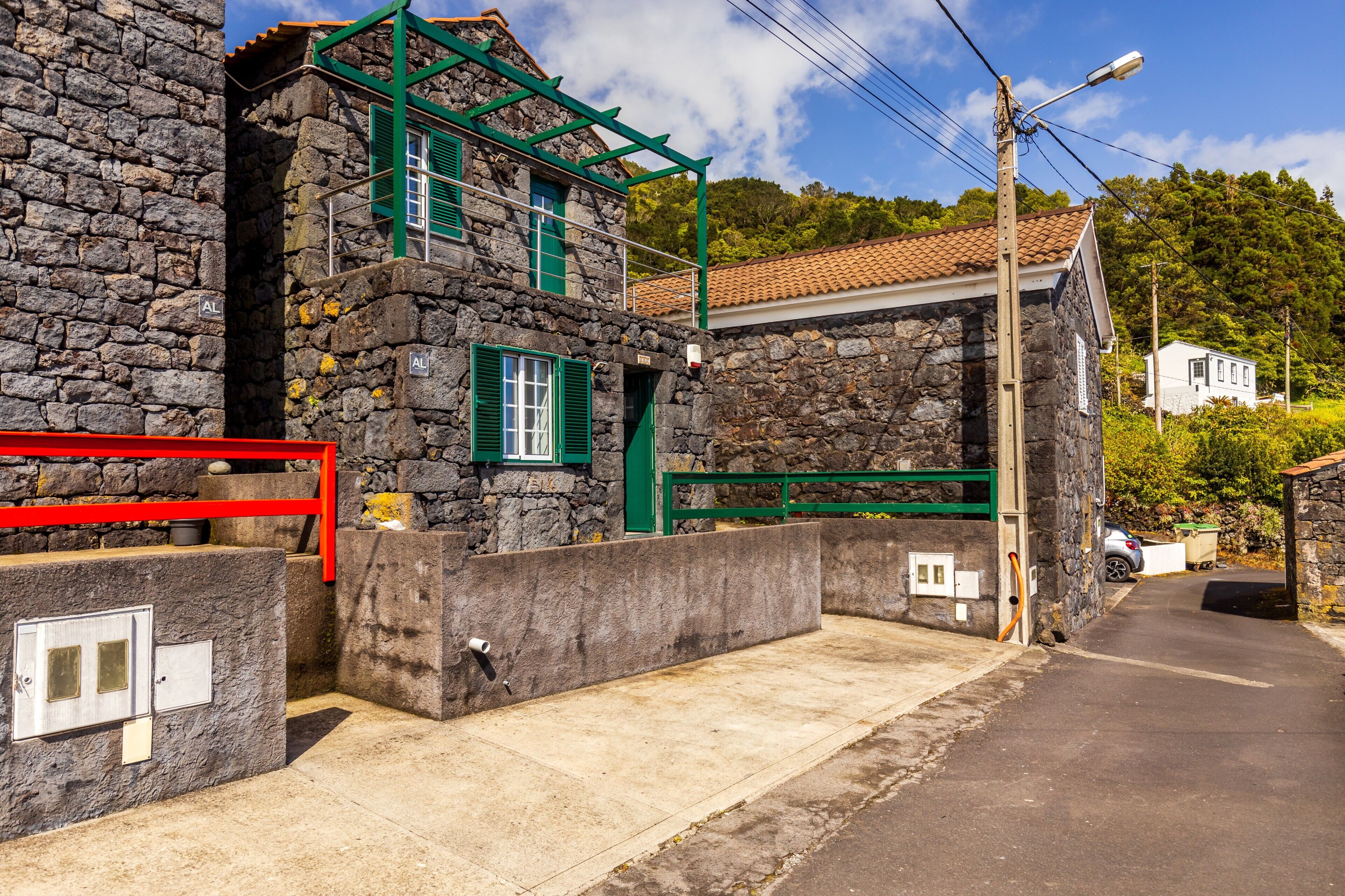 A stone building with a red gate, a metal door, and a small window with green shutters.