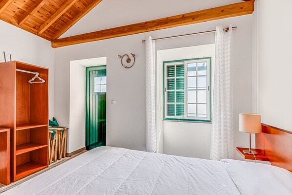 Ein Schlafzimmer mit Holzboden, einem Bett, einem Kleiderschrank, einem Fenster mit Rollläden und einem Nachttisch mit Lampe.