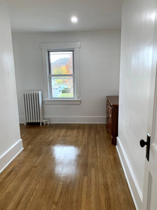 A room with hardwood flooring, a window with a view of trees, a radiator, and a wooden cabinet. - Spacious Port Jervis Home - beautiful views (Port Jervis)