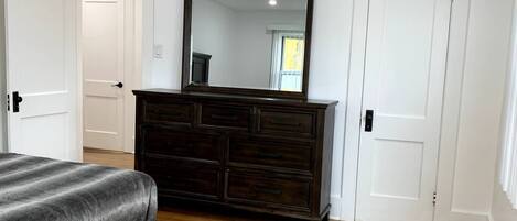 A bedroom with a wooden floor, a dark wooden dresser, a large mirror, and white doors.