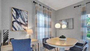 A modern dining area with a round table, blue and grey chairs, a lamp, and abstract art on the walls. - Stunning 2/2 dream beach getaway in Surfside (Surfside)