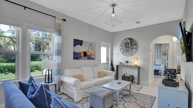 A modern living room with a white sofa, a coffee table, and a large clock on the wall. - Stunning 2/2 dream beach getaway in Surfside (Surfside)