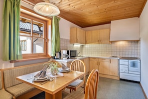 A cozy kitchen with wooden cabinets, a dining table with chairs, a microwave, and a stove.