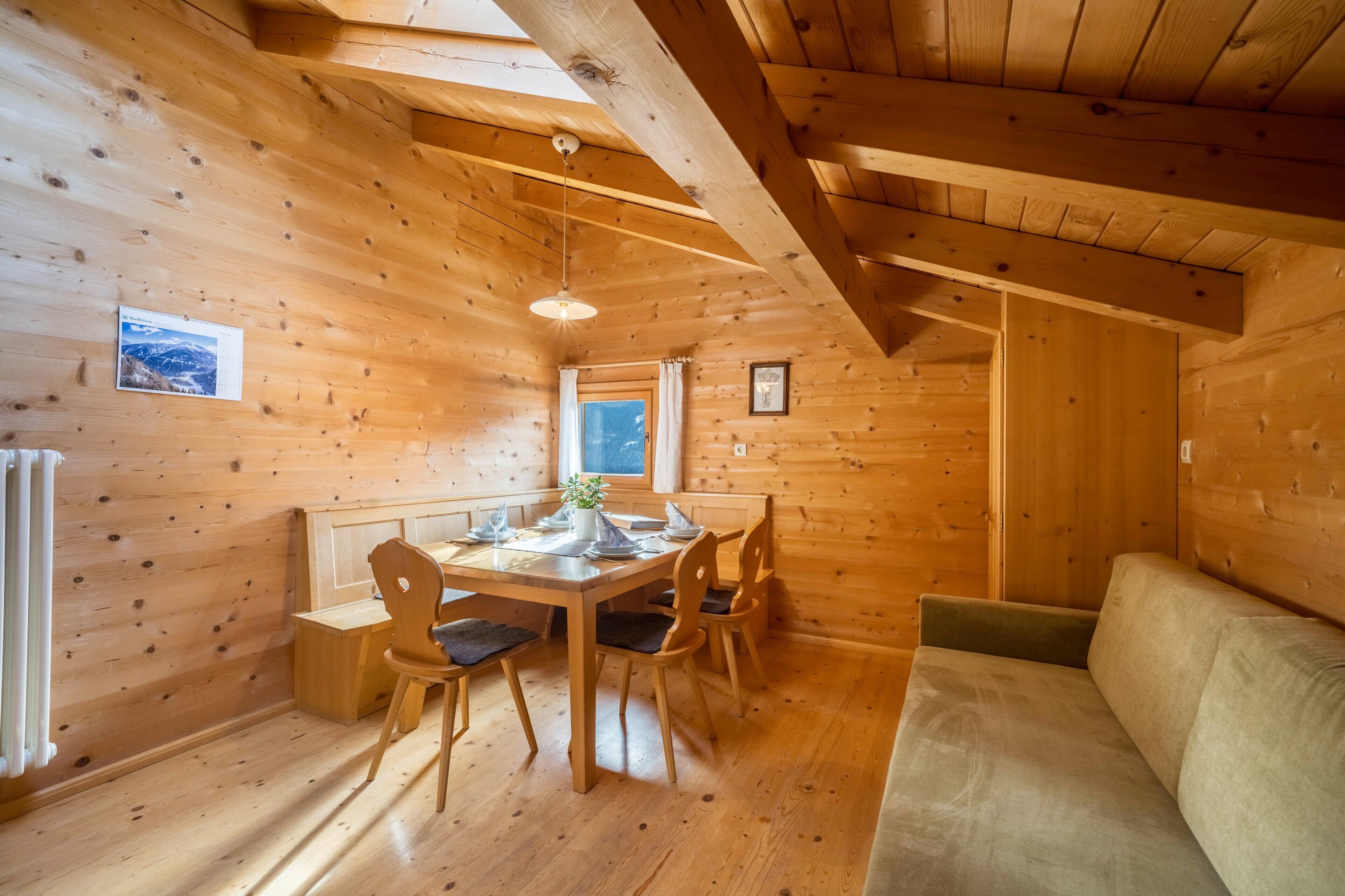 Interior de una cabaña de madera con una mesa de comedor, sillas, un sofá y una ventana.