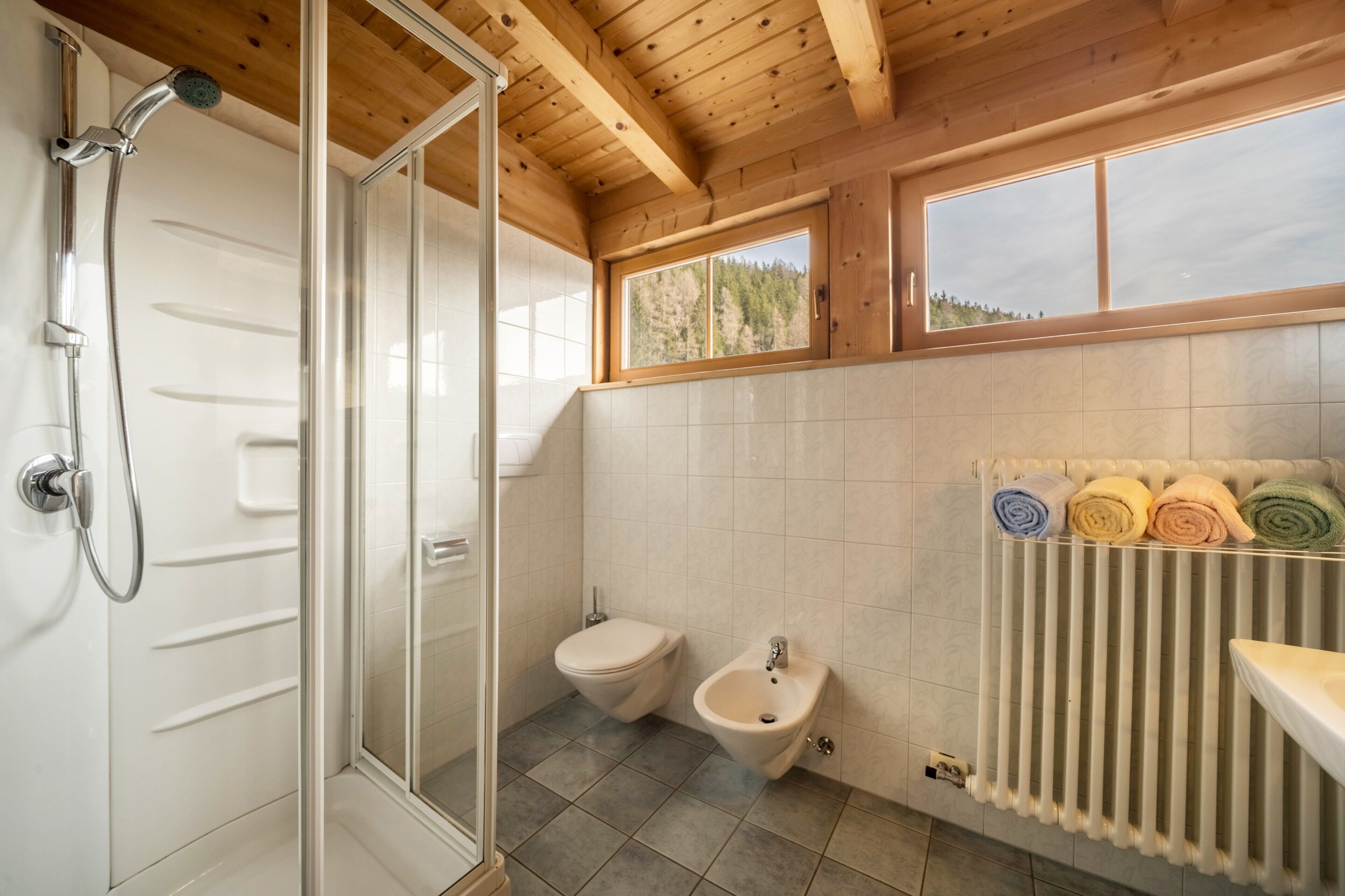 Une salle de bain équipée d’une douche, de toilettes, d’un bidet et d’une fenêtre donnant sur la verdure.