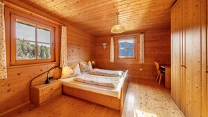 Quarto de cabana de madeira com uma cama de casal, uma escrivaninha e uma cadeira.