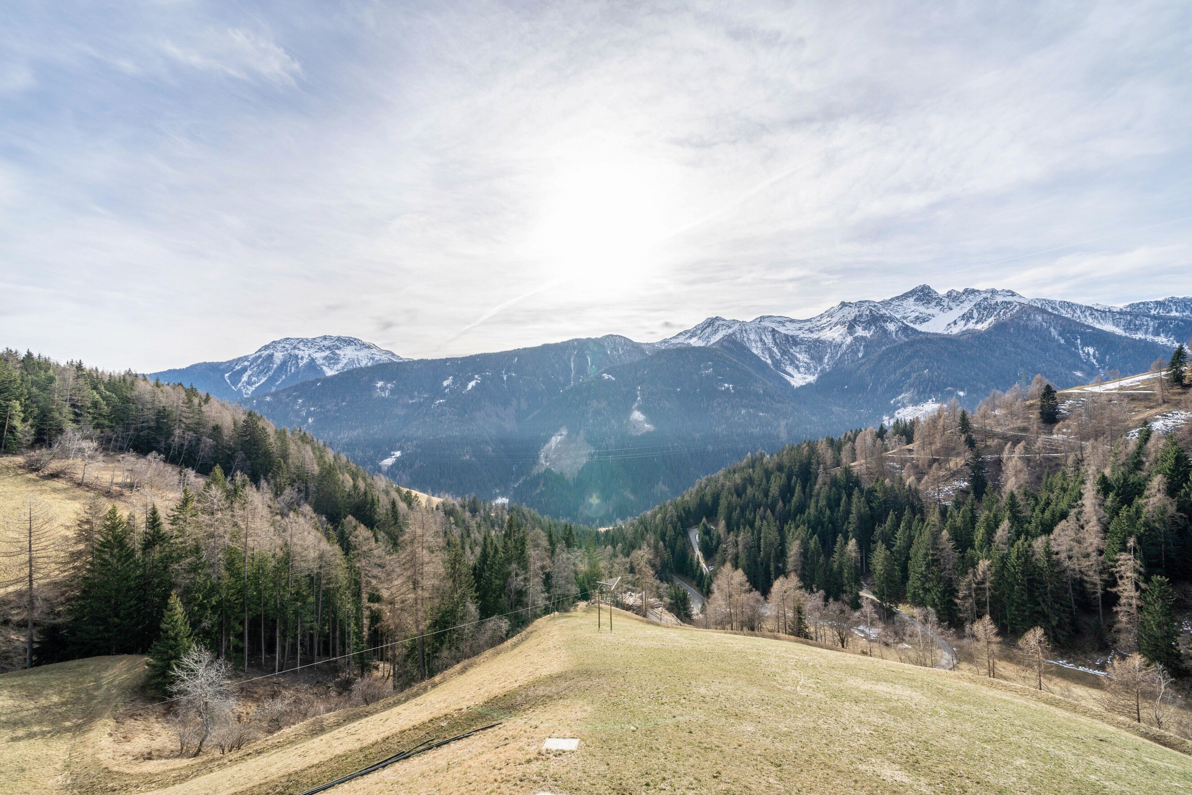 A mountainous landscape with a clear sky, a valley, and a road leading towards the mountains.