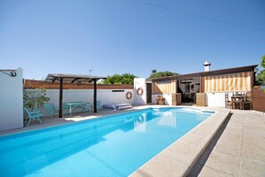 Een zwembad met een zonnescherm, buitenmeubels en een klein terras.