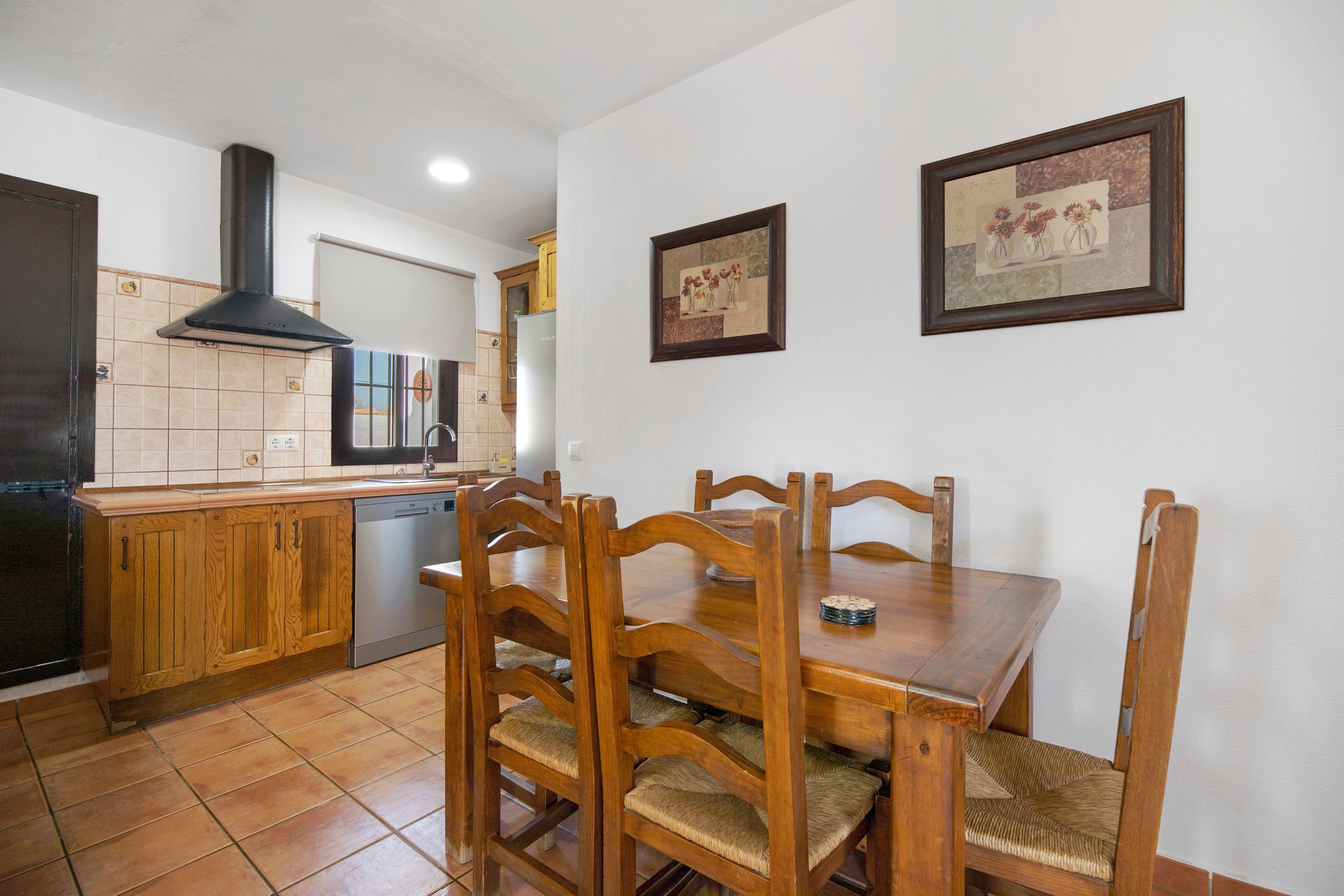 Une cuisine avec des meubles de rangement en bois, une cuisinière et une table à manger avec des chaises.