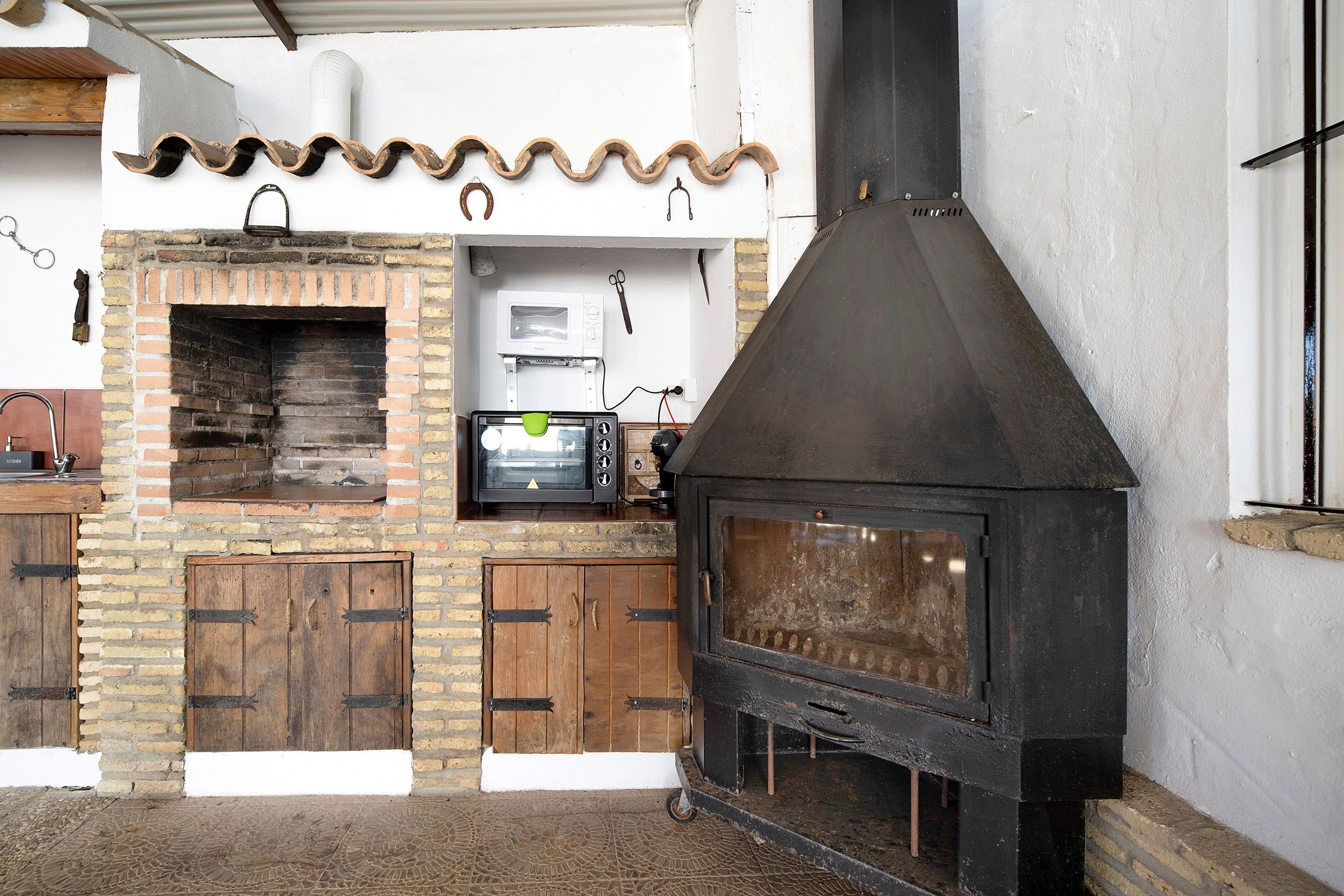 Una cocina con horno de ladrillo, microondas y estufa de leña negra.