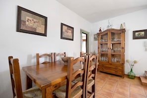 A dining room with a wooden table and chairs, a cabinet with glassware, and framed artwork on the walls.