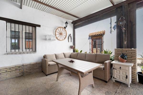 Ein überdachter Patio-Bereich mit einer Rattan-Couch, einem Holztisch und einem weißen Schrank.