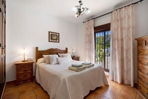 Een slaapkamer met een houten bed, nachtkastje, dressoir en een raam met gordijnen.