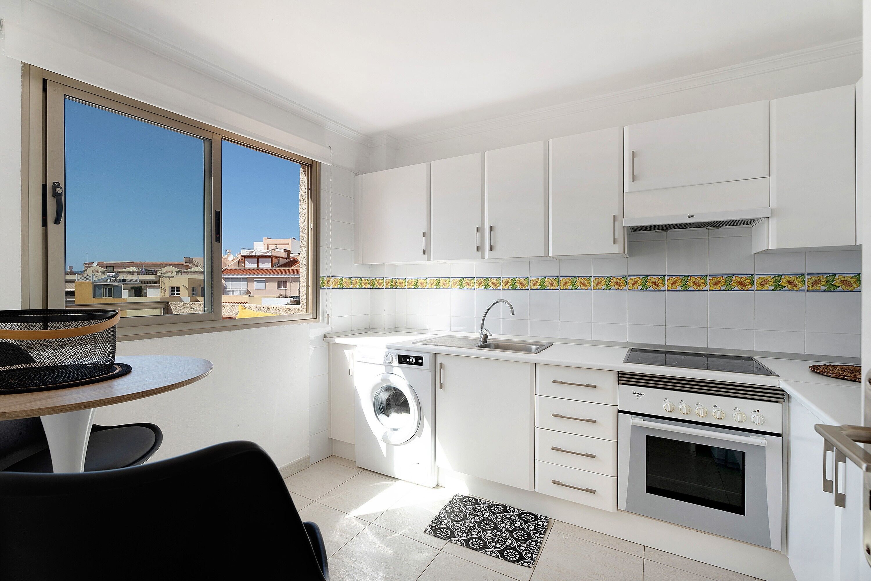 Cocina compacta con lavadora, horno y vistas por una ventana.