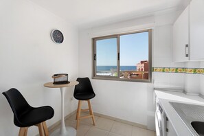 Une cuisine avec une fenêtre, une horloge, deux chaises, une table et un lave-linge.