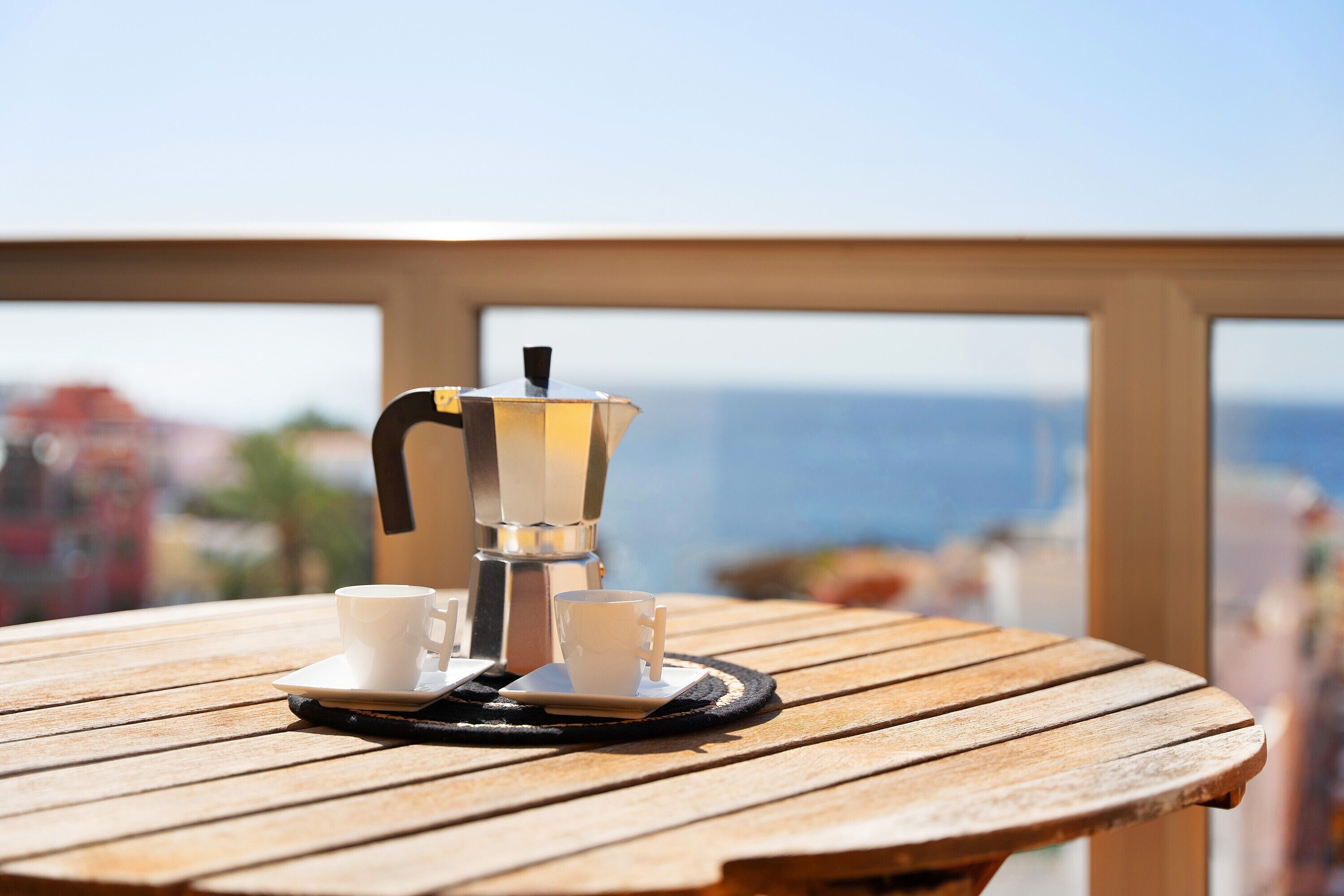 A wooden table with a coffee maker and cups, overlooking a scenic view.