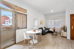 Un salon moderne comprenant un coin repas, un canapé, un téléviseur et une fenêtre donnant sur des immeubles.