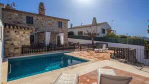 A stone building with a pool, outdoor seating, and a clear sky.