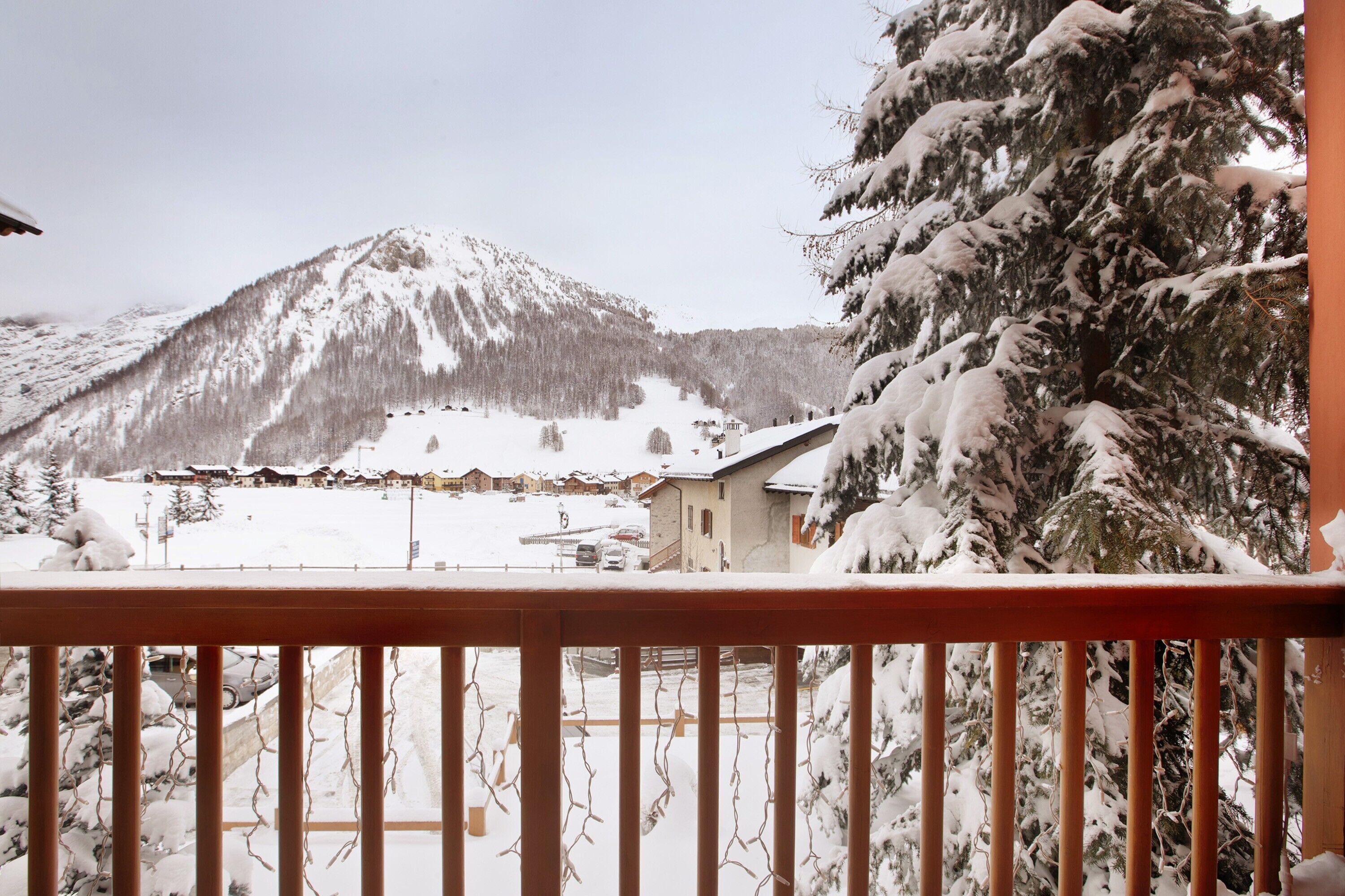 A snowy mountain landscape with a building and trees in the foreground.