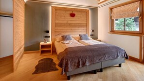 Una camera da letto con testiera in legno, un letto con coperta fantasia, un comodino, una decorazione a forma di cuore rosso e una finestra con tende a motivi.