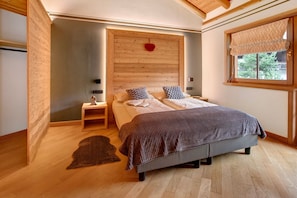 A bedroom with a wooden headboard, a bed with a patterned blanket, a nightstand, a red heart decoration, and a window with a patterned valance.