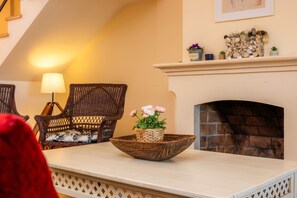 Een kamer met rieten stoelen, een tafel met een geweven schaal, een open haard en een lamp.