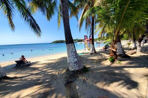 A beach with palm trees, a lifeguard tower, and a person sunbathing.