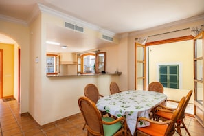 A dining area with a round table, wicker chairs, and a white tablecloth.