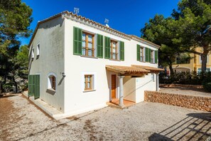 A white building with green shutters, a stone wall, and a gravel driveway.
