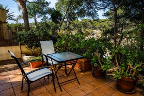 An outdoor patio with a table and chairs, surrounded by potted plants and trees. - Holiday Home 'Cala Pi Two' (Cala Pi)