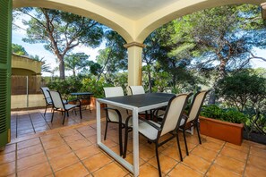 An outdoor patio with a table and chairs, surrounded by trees and a covered area.