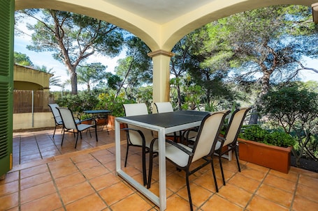 Une terrasse extérieure avec une table et des chaises, entourée d’arbres et dotée d’un espace abrité.. Maison de vacances 'Cala Pi Two'