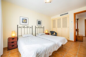 A double bed with a white bedspread, two bedside tables with lamps, a chair, and a wardrobe with louvered doors. - Holiday Home 'Cala Pi Two' (Cala Pi)