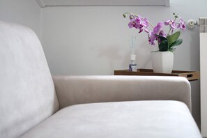 A room with a white chair, a white bedside table, and a white wall.