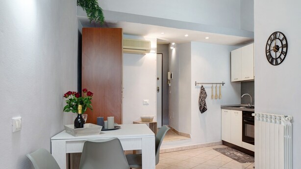 A modern kitchen with white cabinets, a clock, and a dining area with a table and chairs.