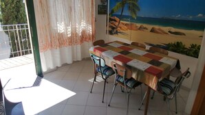 A dining area with a table covered in a checkered tablecloth, chairs, a mural of a beach scene, and a view through a window with a curtain.