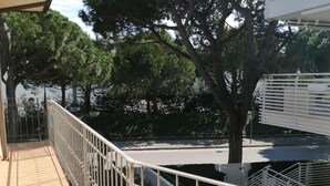 A balcony with a metal railing, a wooden floor, and trees in the background.