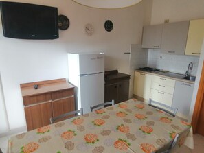 A compact kitchen with a refrigerator, stove, sink, and a dining table with a floral tablecloth.