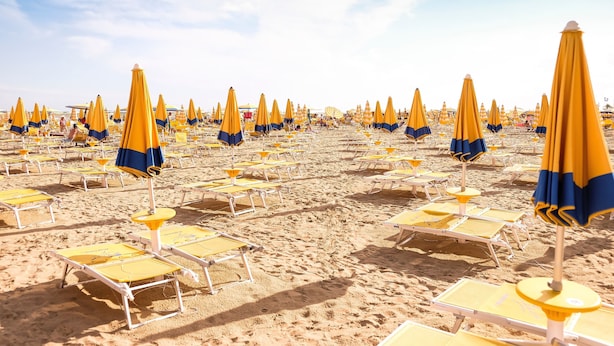 Une plage bordée de rangées de transats et de parasols.