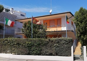 A two-story building with balconies, a satellite dish, and flags.
