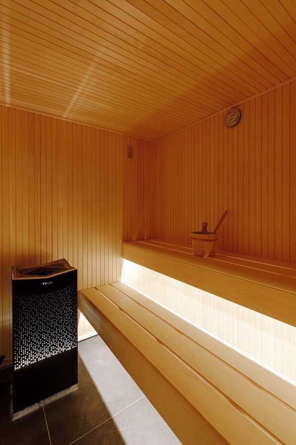 Un sauna con bancos de madera, un calentador y un reloj en la pared.