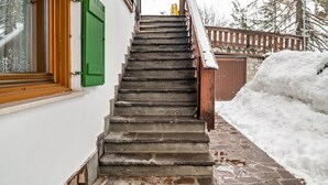 Un escalier menant à une porte en bois, une fenêtre avec des volets verts et une zone recouverte de neige.