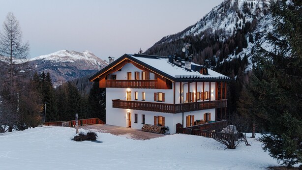 Un chalet à deux étages doté d’un balcon, entouré de neige et de montagnes.