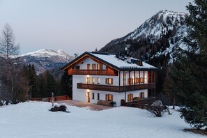 Un chalet de dos pisos con balcón, rodeado de nieve y montañas.