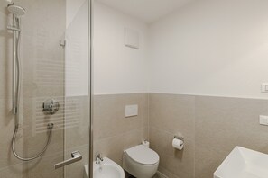 Ein Badezimmer mit Duschkabine aus Glas, Toilette, Bidet und Waschbecken.