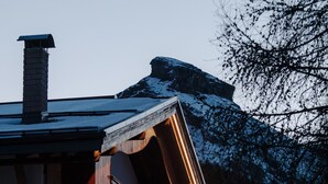 Un immeuble à plusieurs étages doté d’un balcon et d’une cheminée, avec une montagne enneigée en arrière-plan.